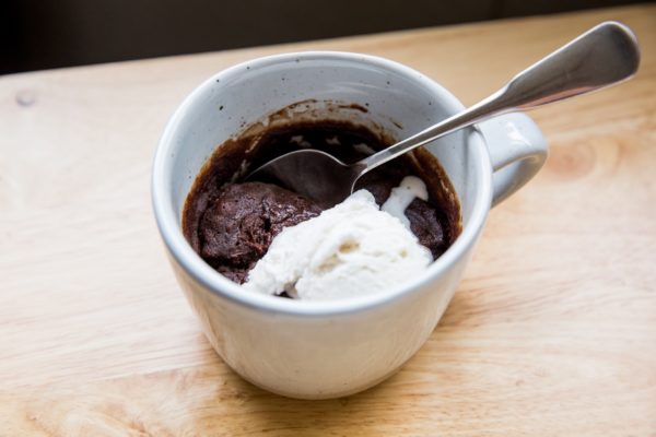 Horizontal image of a mug of brownie and ice cream sitting on a wooden table.