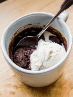 Close up shot of a finished brownie in a mug with a small scoop of vanilla ice cream on top, ready to eat.