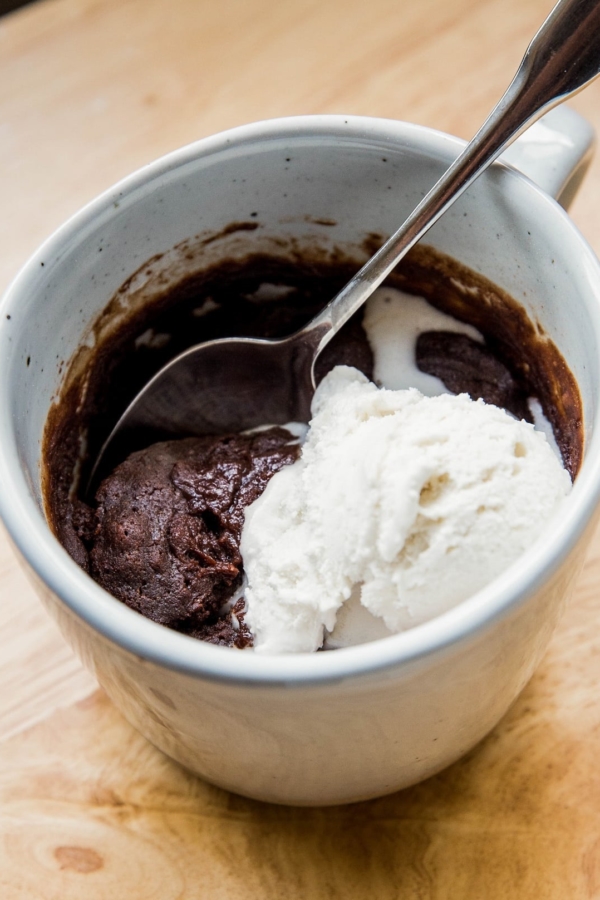 Close up shot of a finished brownie in a mug with a small scoop of vanilla ice cream on top, ready to eat.