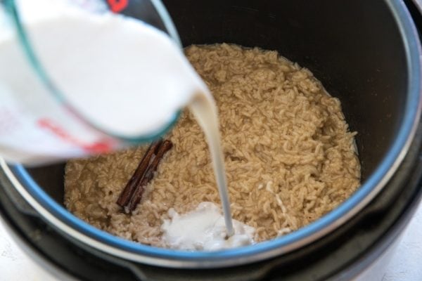 Pouring coconut milk into an Instant Pot with rice pudding inside to make it extra creamy.