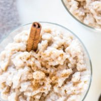 Top down close up photo of two dessert bowls of creamy rice pudding with a napkin and two spoons to the side.