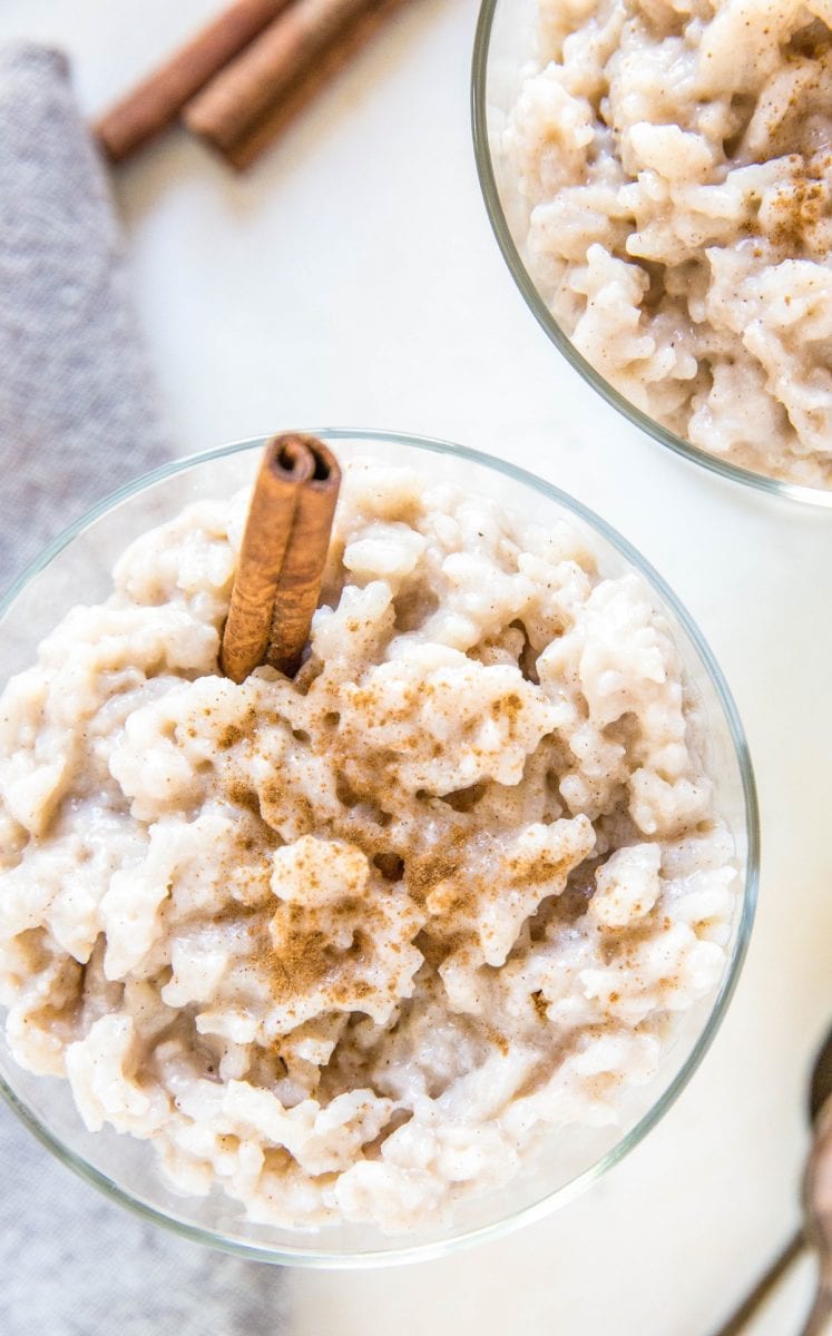 Top down close up photo of two dessert bowls of creamy rice pudding with a napkin and two spoons to the side.