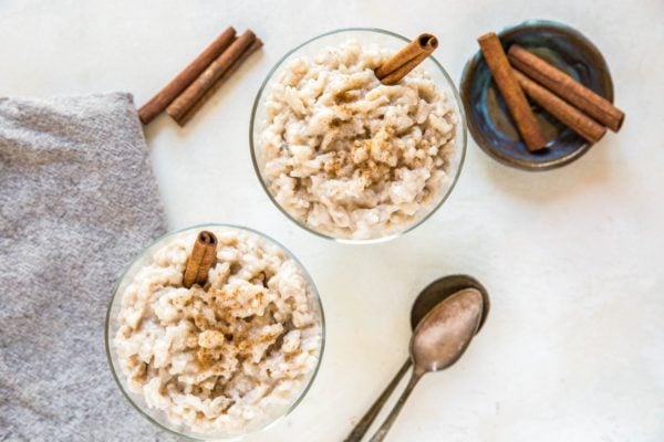 Horizontal image of two bowls of rice pudding with a sprinkle of cinnamon and a cinnamon stick inside. Two spoons to the side, ready to eat.