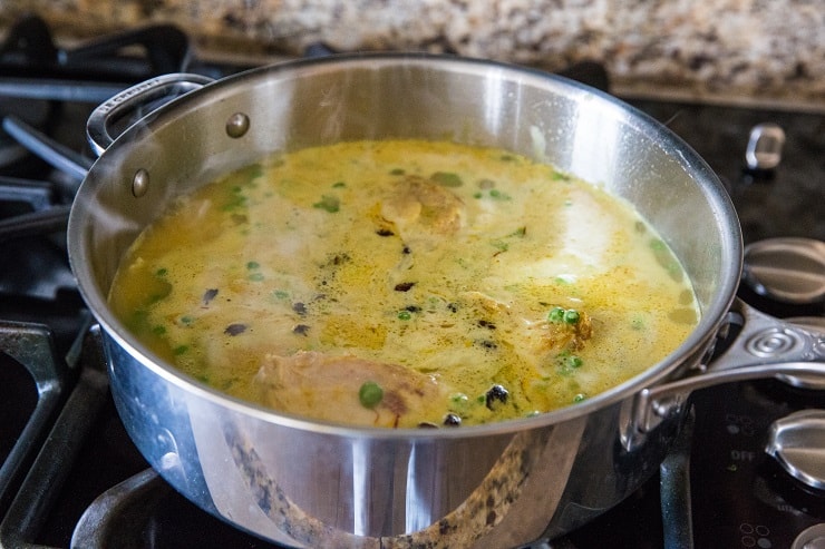 Cooking saffron chicken in a large skillet with coconut milk marinade and rice