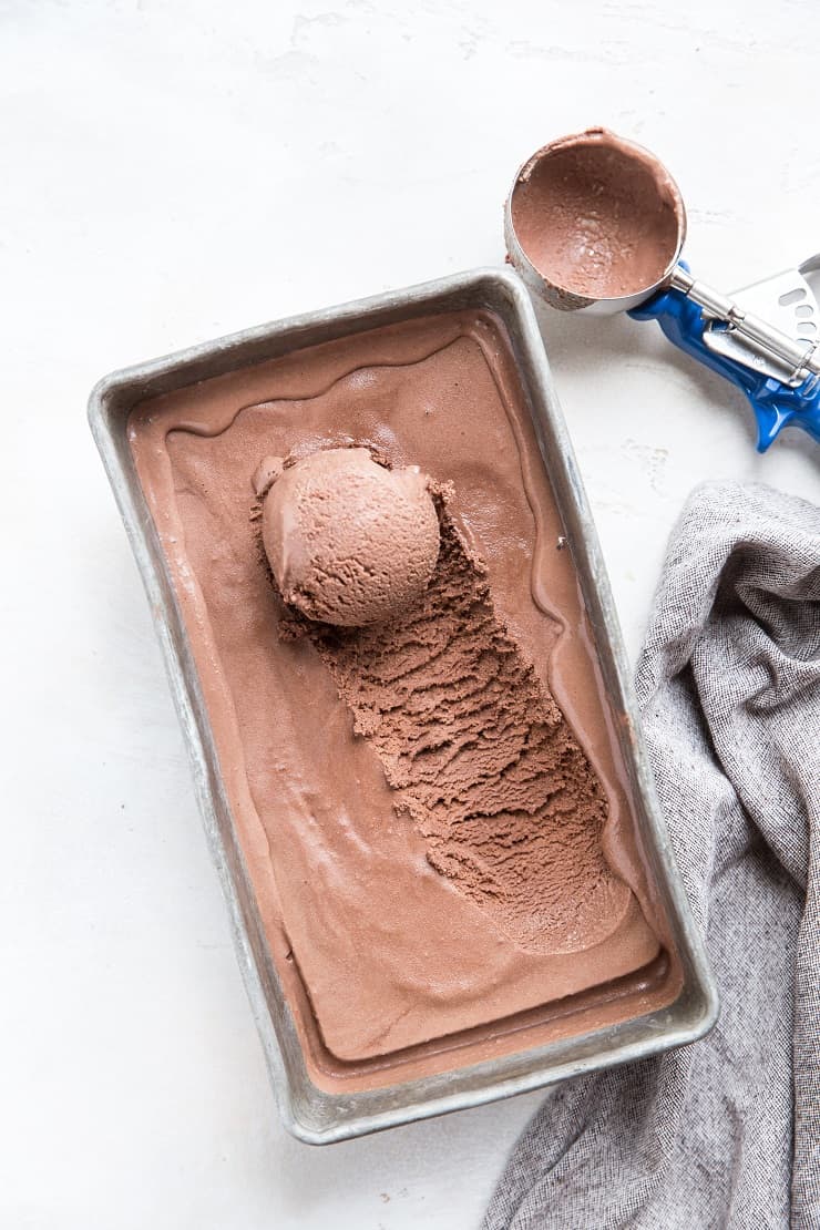 loaf pan with chocolate ice cream with a scoop taken out and an ice cream scooper to the side