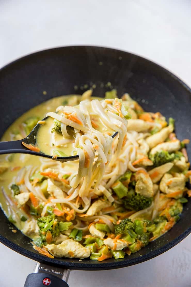 large wok with curry noodles with spoon scooping out some of the noodles