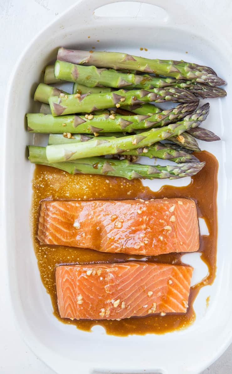 Raw salmon and asparagus in a casserole dish with asian marinade