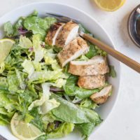 Balsamic Baked Chicken Caesar Salad in a bowl with a napkin and half a lemon