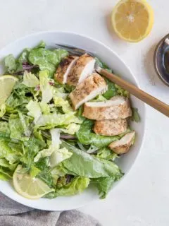 Balsamic Baked Chicken Caesar Salad in a bowl with a napkin and half a lemon