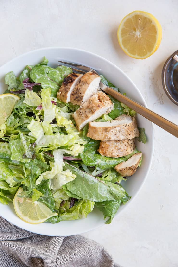 Balsamic Baked Chicken Caesar Salad in a bowl with a napkin and half a lemon