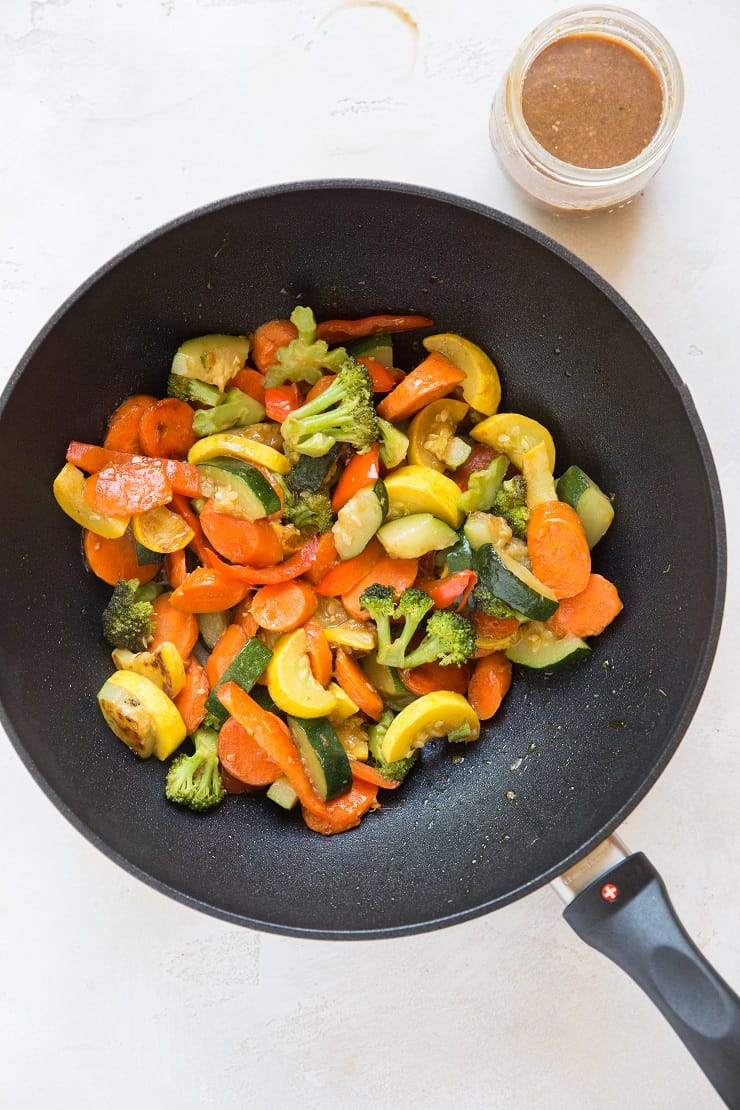 Wok of stir fry vegetables with jar of sauce next to it