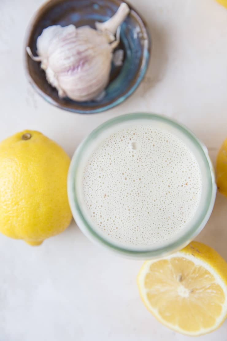 Top down photograph of jar of Caesar salad dressing with lemons and garlic to the side