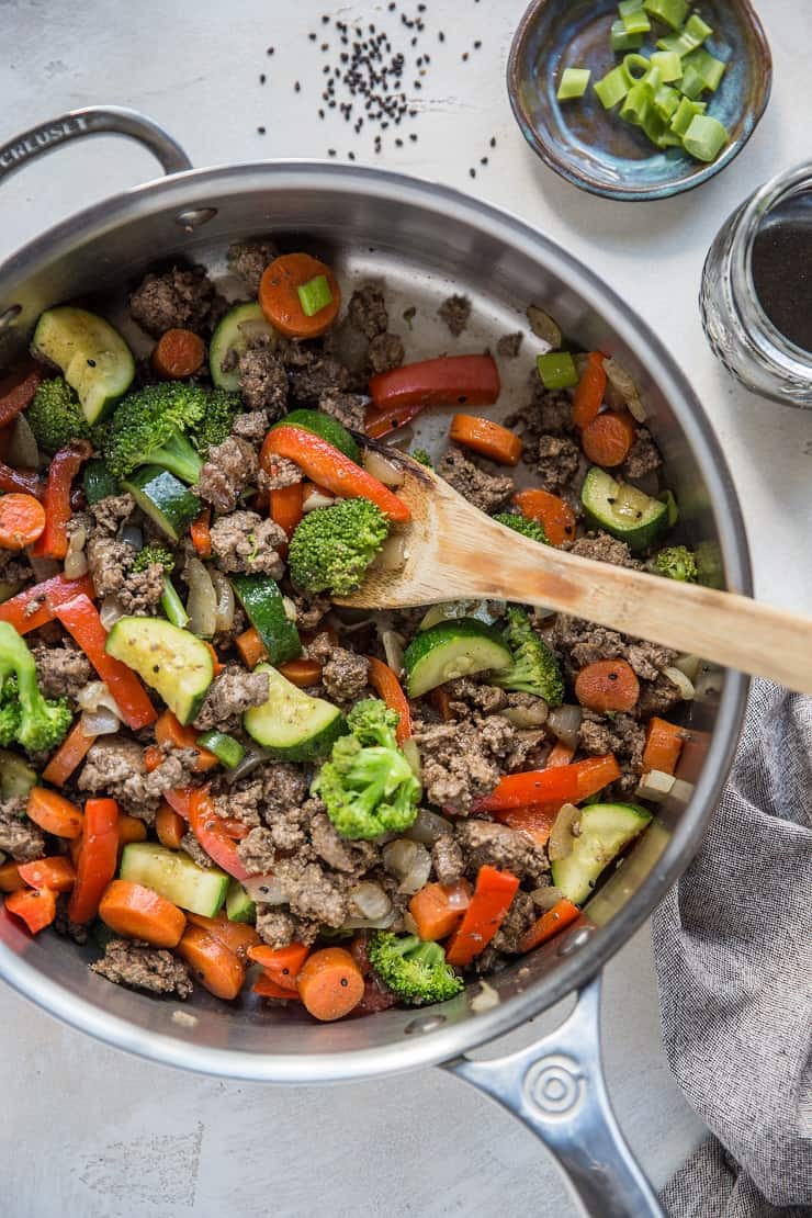 30-Minute Teriyaki Beef Skillet with Vegetables sitting on a white backdrop with jar of teriyaki sauce and a wooden spoon