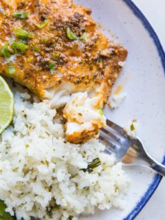 Fish on a plate with a bite taken out of it with a fork. Cauliflower rice to the side.