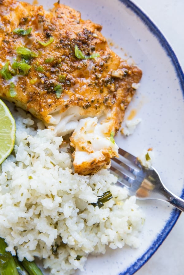 Fish on a plate with a bite taken out of it with a fork. Cauliflower rice to the side.