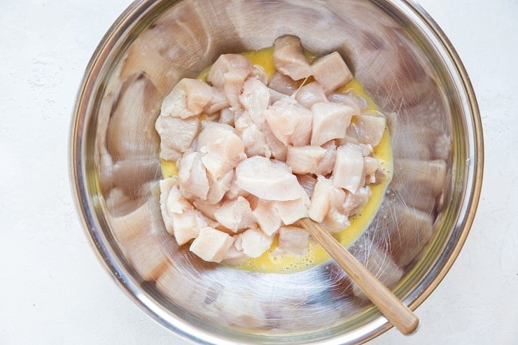 chopped raw chicken in a mixing bowl with beaten egg