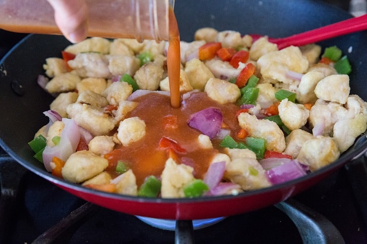 Pouring sweet and sour sauce into skillet with chicken and vegetables