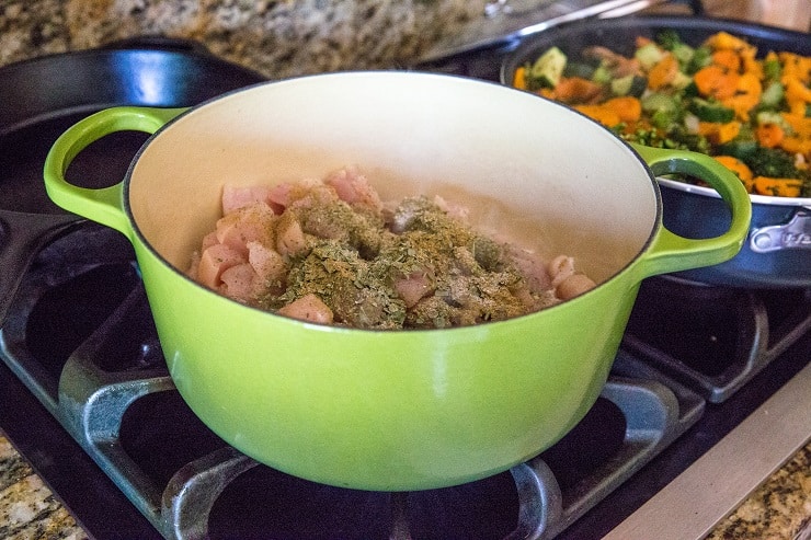Raw chopped chicken cooking in a dutch oven with seasonings