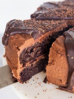 Close up of a thick slice of chocolate cake being cut out of the full cake, about to be served.