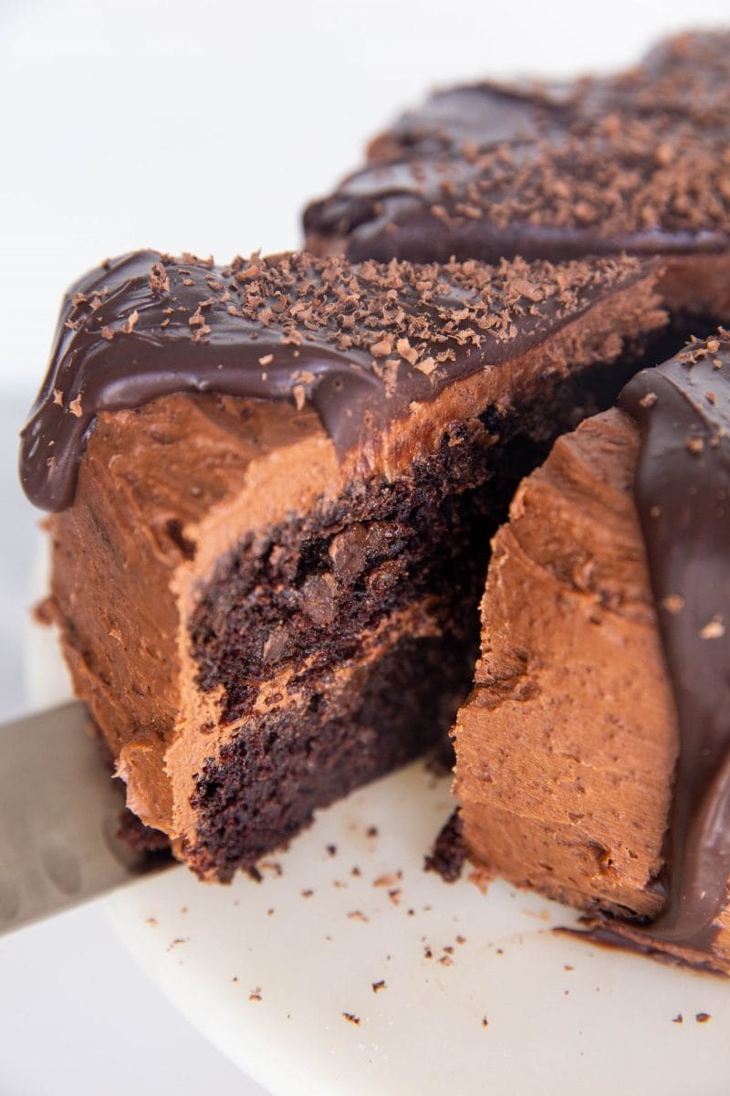 Close up of a thick slice of chocolate cake being cut out of the full cake, about to be served.