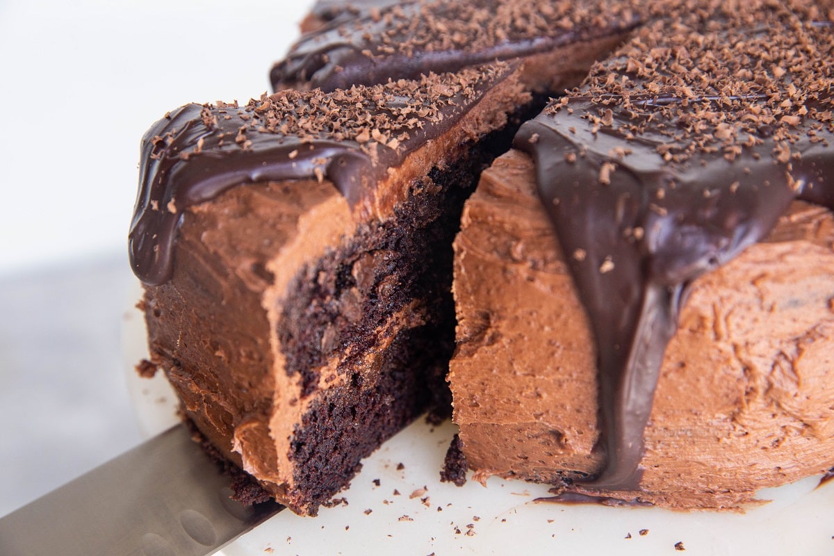 Slice of chocolate cake being cut out of a full cake with a knife.