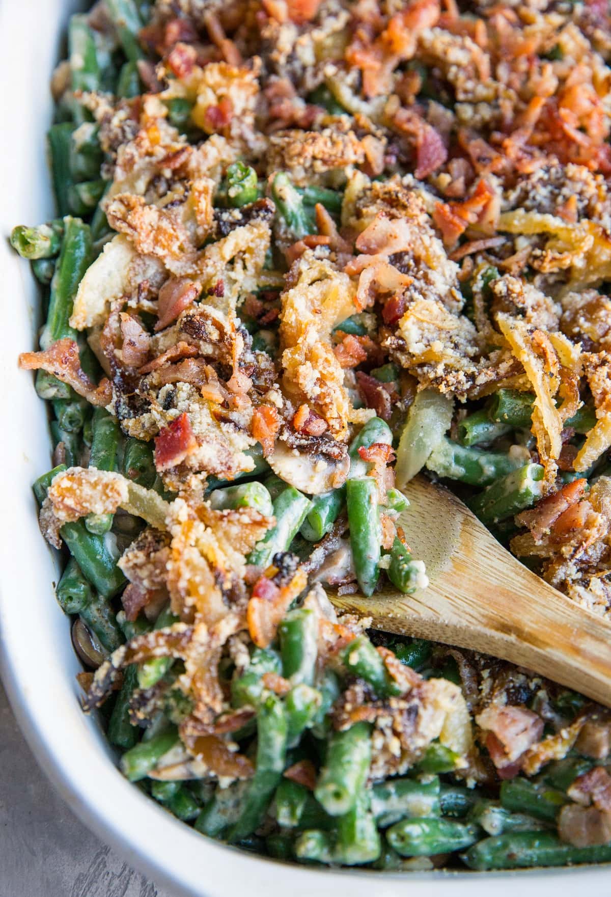 Close up image of wooden spoon taking a scoop of green bean casserole out of a casserole dish, ready to serve.