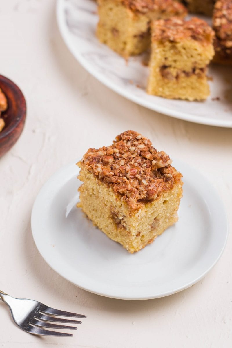 Slice of coffee cake on a plate with a fork to the side and more slices on a plate in the background.