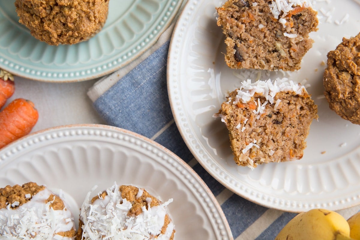 Top down photo of a healthy carrot cake muffin sliced in half sitting on a dark blue plate with a golden napkin