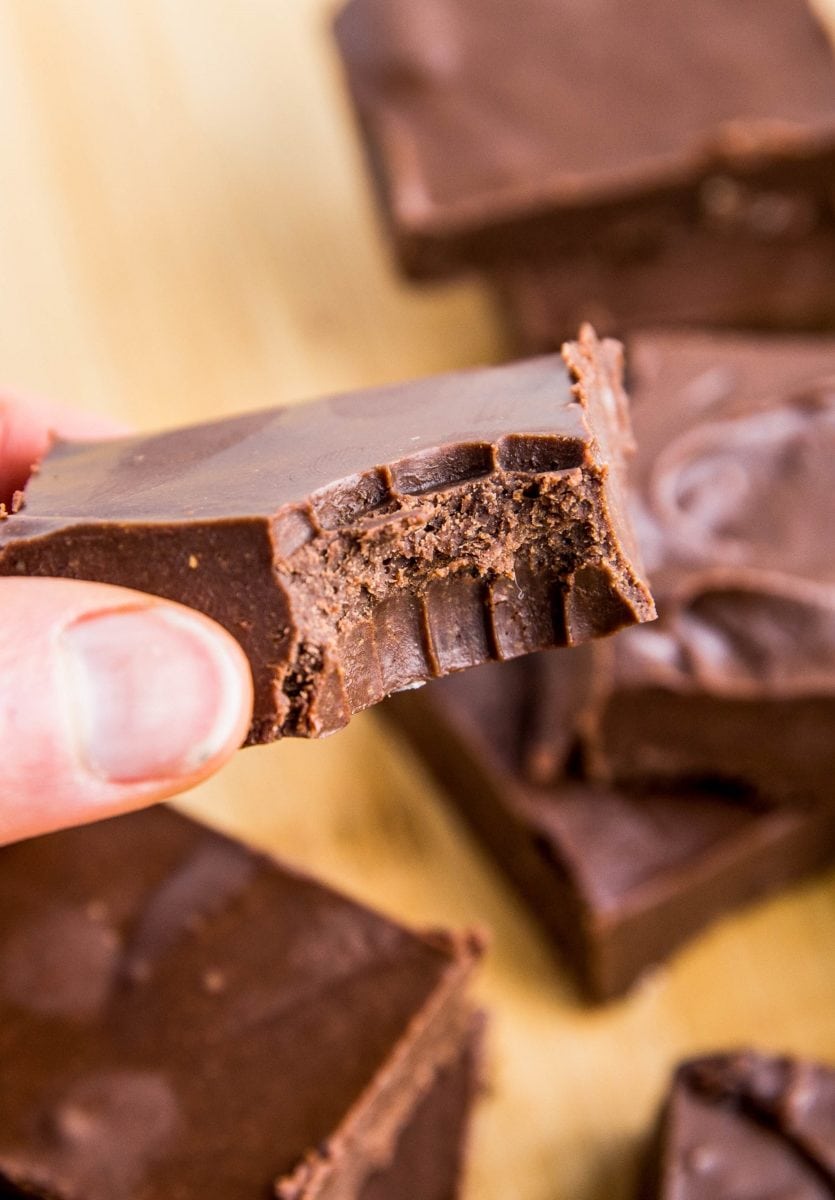 Hand holding a square of fudge with a bite taken out.