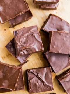 Top down photo of chunks of chocolate fudge sliced up on a wooden cutting board.