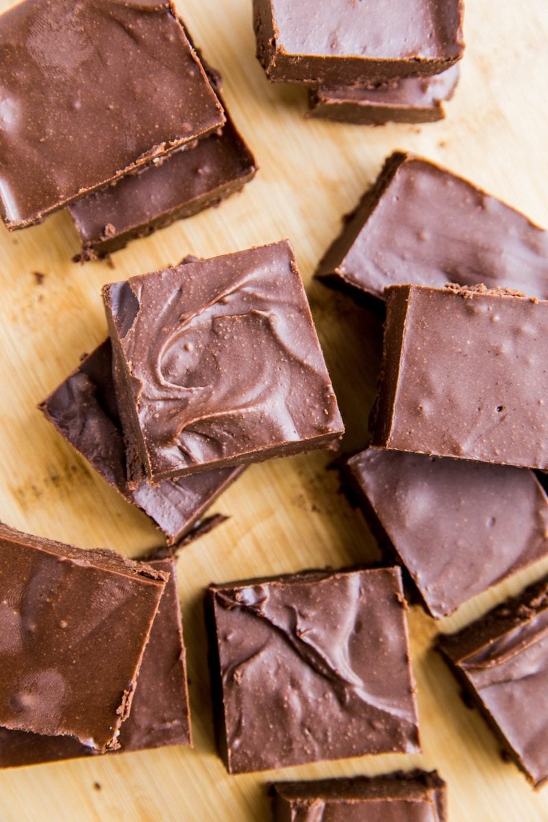 Top down photo of chunks of chocolate fudge sliced up on a wooden cutting board.