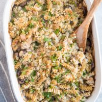 Finished tuna noodle casserole on a blue backdrop with a napkin to the side. Crispy topping and fresh parsley sprinkled on top.