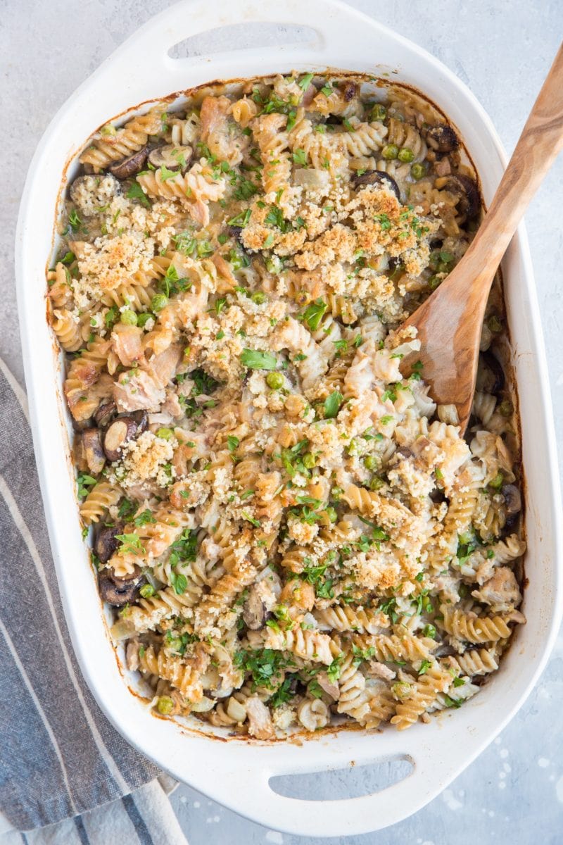 Finished tuna noodle casserole on a blue backdrop with a napkin to the side. Crispy topping and fresh parsley sprinkled on top.