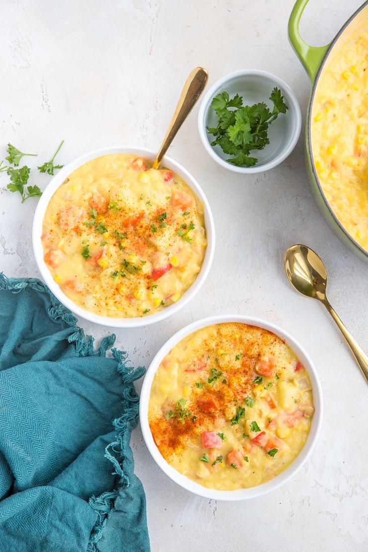 Two bowls of vegan corn chowder next to a pot of vegan corn chowder