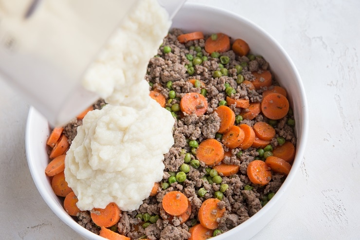 Pouring mashed cauliflower over meat mixture to make meat pie