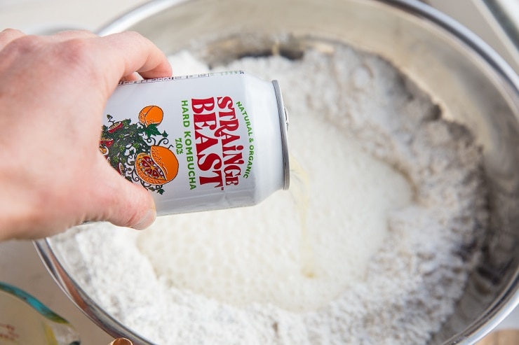 Pouring kombucha into a mixing bowl with flour to make bread