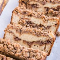 Loaf of Paleo Cinnamon Swirl Banana Bread cut into slices on a wood cutting board. Grain-Free, dairy-free, refined sugar-free healthy banana bread with streusel topping. Delicious gluten-free recipe for breakfast or snack.