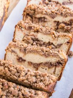 Loaf of Paleo Cinnamon Swirl Banana Bread cut into slices on a wood cutting board. Grain-Free, dairy-free, refined sugar-free healthy banana bread with streusel topping. Delicious gluten-free recipe for breakfast or snack.