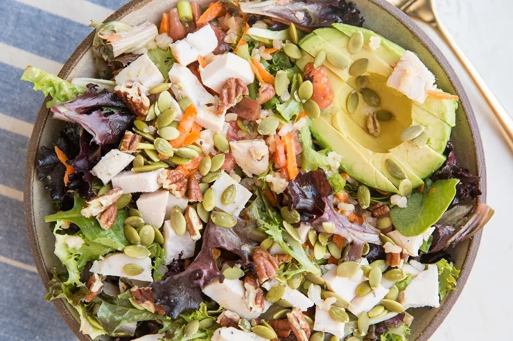 A filling, nutritious salad recipe with spring greens, chicken, avocado, carrots, heirloom tomato, pumpkin seeds, pecans, and more!