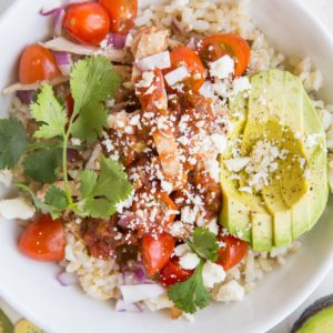 Big Chicken Burrito Bowl with a flower napkin and avocado to the side. Topped with delicious burrito bowl toppings.