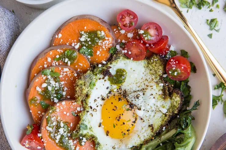 Pesto Eggs with Sweet Potatoes, Greens, and cherry tomatoes and feta cheese. A delicious breakfast bowl!