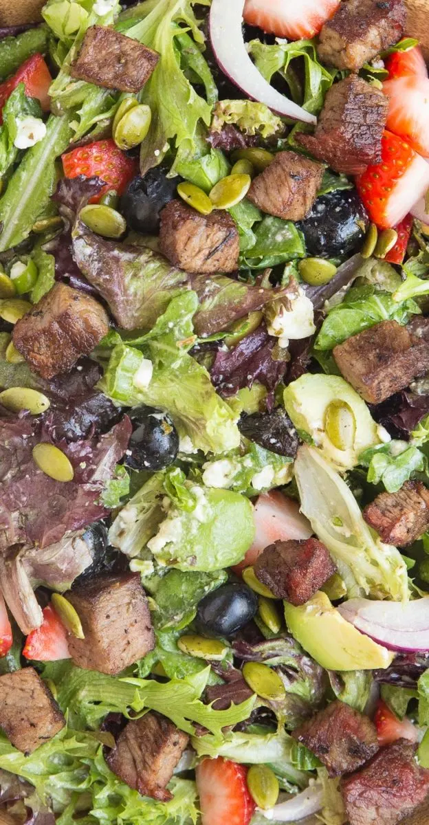 Amazingly flavorful Steak Salad with sweet tangy berries, creamy avocado and feta, Green Goddess Dressing, red onion, green onion, and pumpkin seeds. A unique and delicious healthy salad recipe!