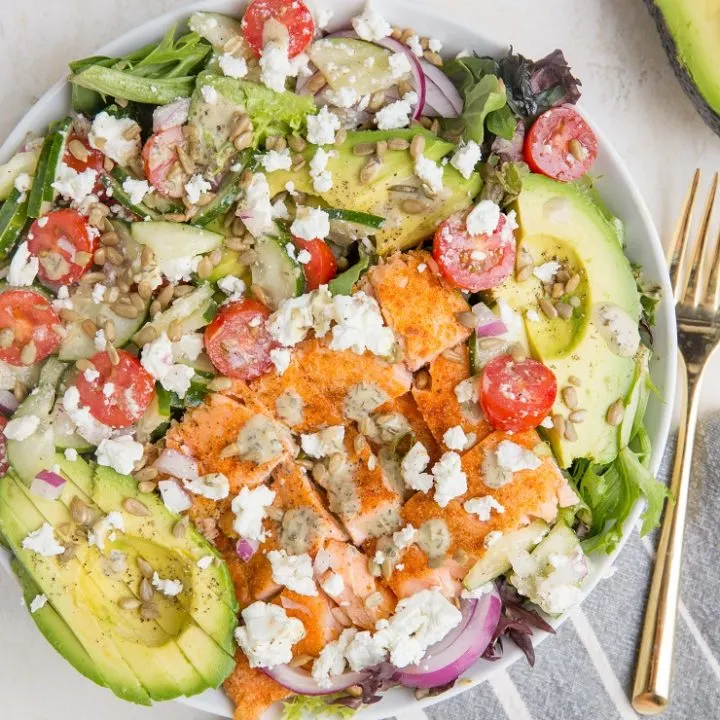 Greek Salmon Salad with spring greens, avocado, feta, sunflower seeds, cucumber, tomatoes, and an herby delicious dressing. Low-carb, delicious summer salad recipe.
