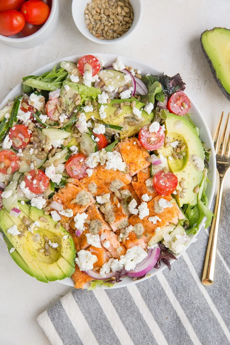 Greek Salmon Salad with spring greens, avocado, feta, sunflower seeds, cucumber, tomatoes, and an herby delicious dressing. Low-carb, delicious summer salad recipe.