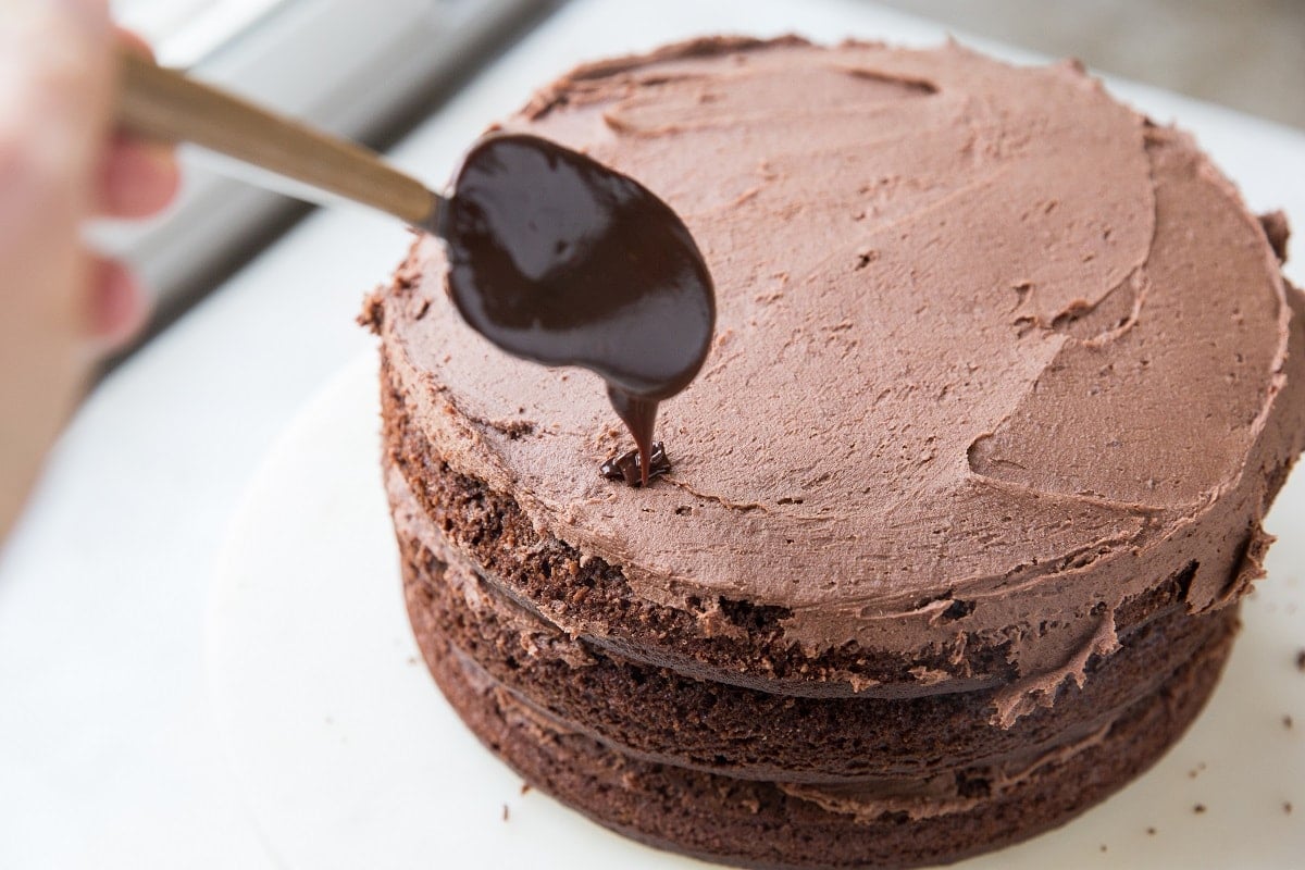 Hand drizzling ganache over a frosted chocolate cake