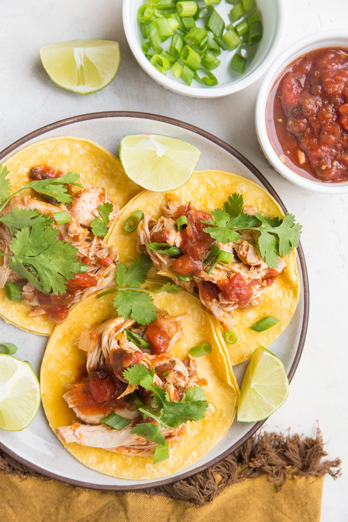 Plate of shredded chicken tacos with cilantro on top and a golden napkin to the side.