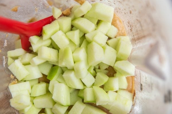 Blender with cake batter in it and fresh chopped apples on top, ready to be mixed in.