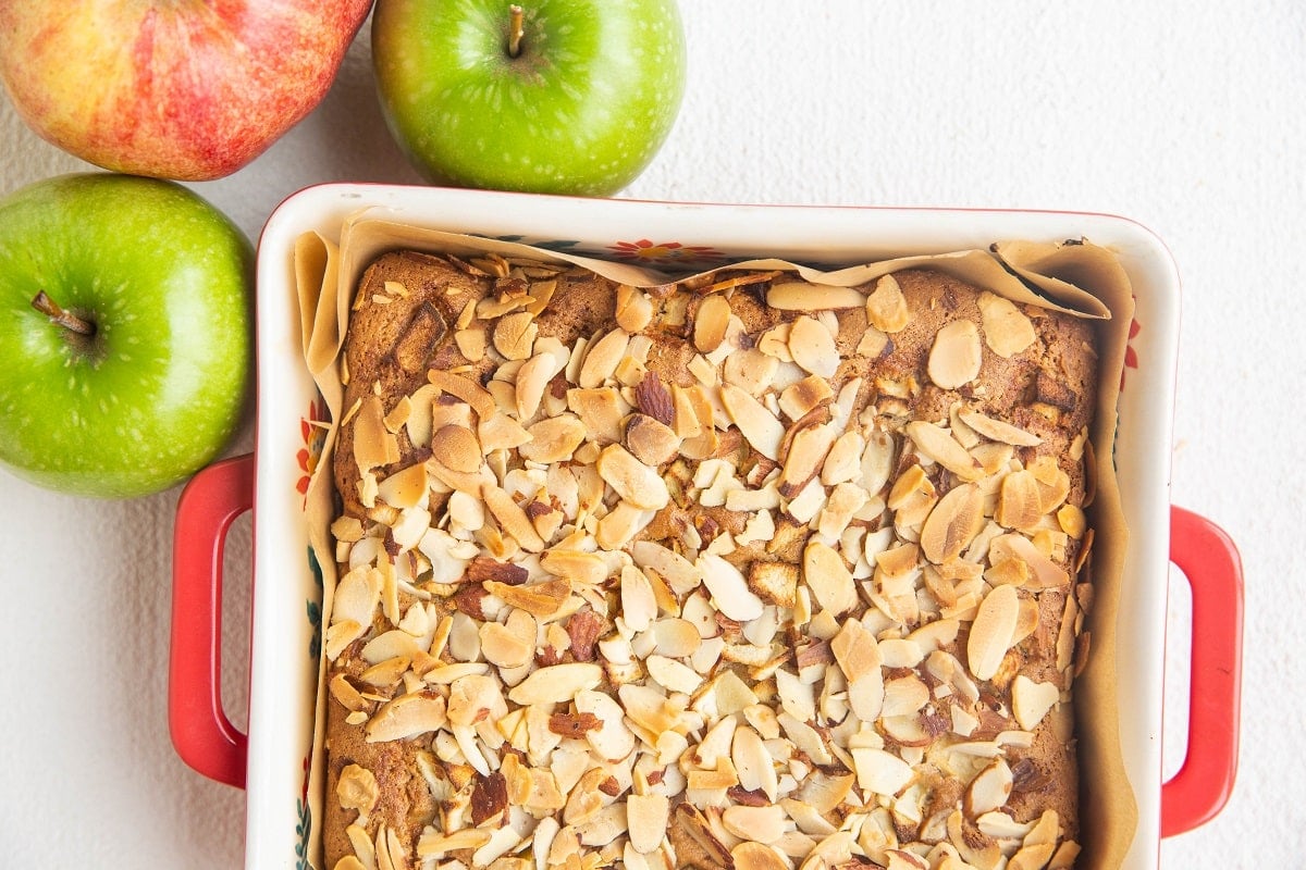 Finished apple cake in a baking dish, fresh out of the oven with fresh apples to the side.