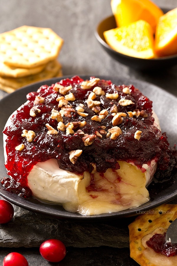 The easiest snack you can make for entertaining holiday guests – Cranberry Baked Brie served on a festive cheese board with crackers and fruit. Great recipe to use up leftover cranberry sauce. Ooey gooey cheese ready in 10 minutes!