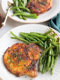 Air Fryer Pork Chops and air fryer green beans together on a white plate with a gold fork, ready to serve. Blue napkin to the side.